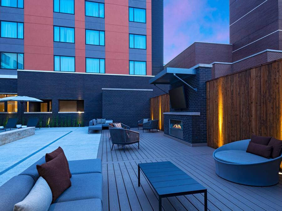 A modern outdoor lounge area with a wooden deck, seating arrangements, and a fireplace.