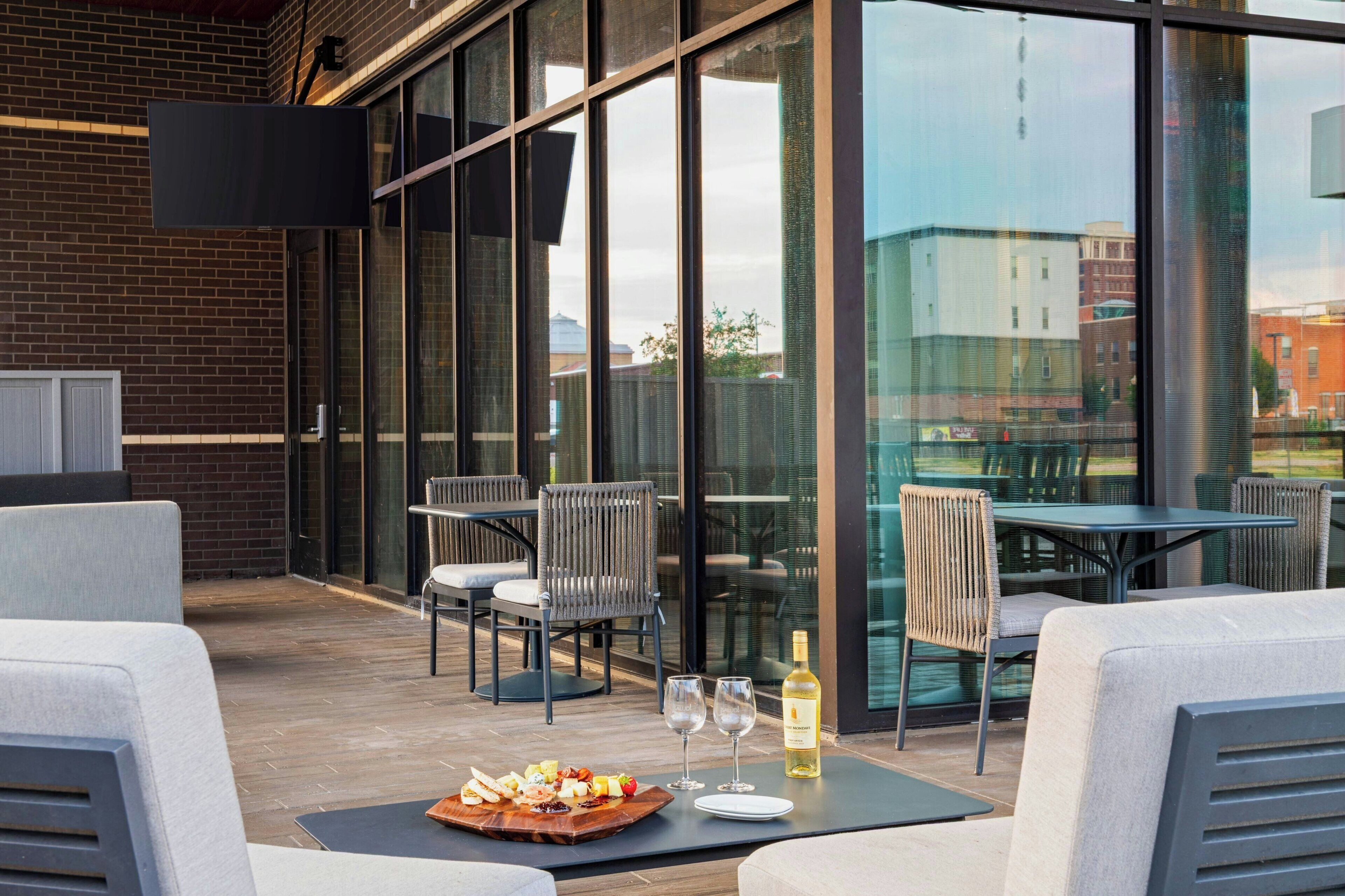 An outdoor seating area with tables and chairs, a wooden board with food, and a bottle of wine.