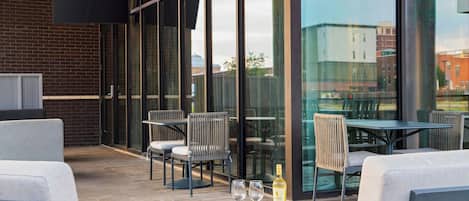 An outdoor seating area with tables and chairs, a wooden board with food, and a bottle of wine.