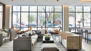 Un vestíbulo moderno con un sofá modular, sillones y una mesita de centro. Amplias ventanas dejan ver coches aparcados y árboles al exterior.