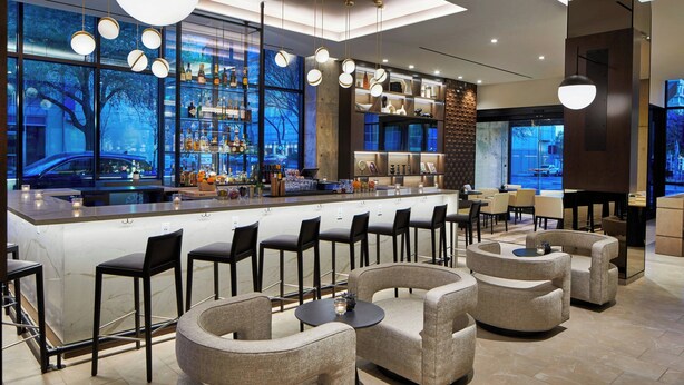 Zona de bar moderna con una barra larga, varios taburetes y un espacio de estar con sofás.