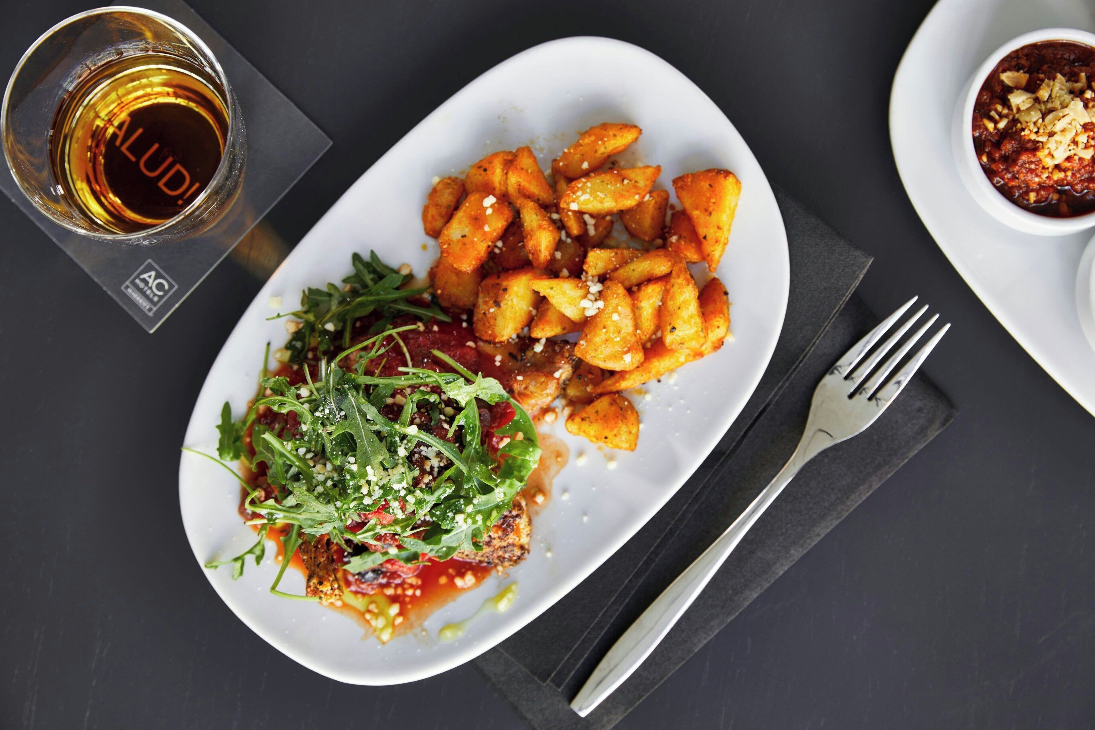 A plate of food with a glass of beer and a fork on a dark surface.