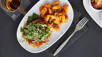 A plate of food with a glass of beer and a fork on a dark surface.