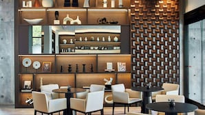 Un interior moderno con una zona de estar central, una pared decorativa con patrones geométricos y estantes mostrando diversos objetos.