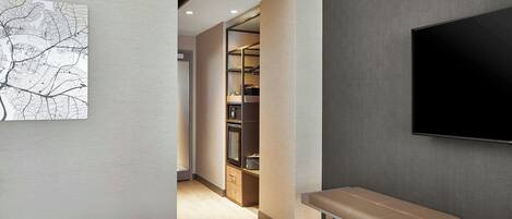 A modern hotel room with a bed, a bench, a TV, and a walk-in closet.