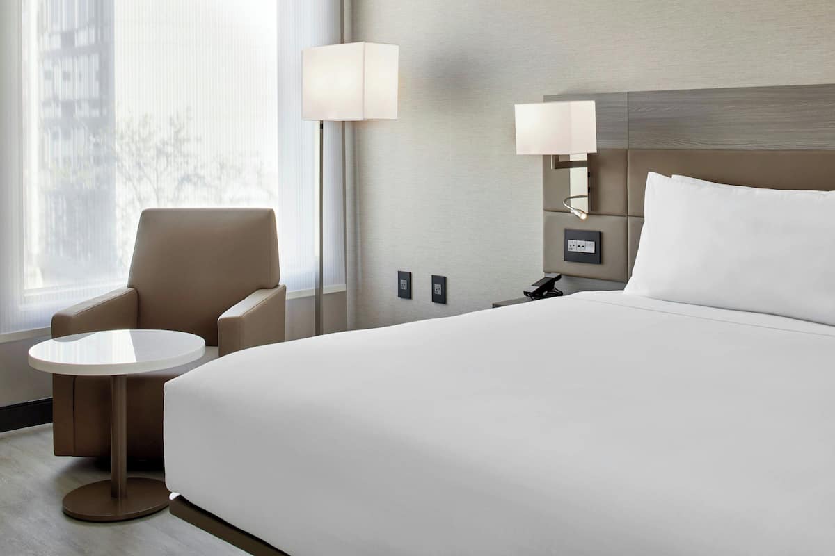 Een hotelkamer met een groot bed, een ronde tafel, een stoel en twee bedlampjes.