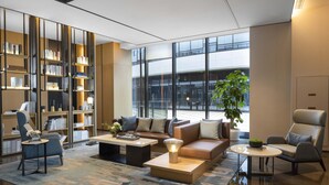 A modern lobby with a large bookshelf, comfortable seating, a coffee table, and a large window offering a view of the outside.