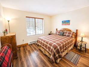 A bedroom with a bed, a desk, a lamp, a window, and a wall sign.