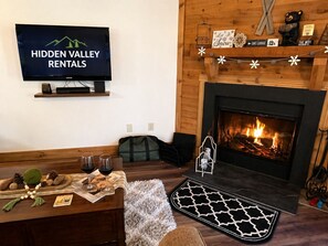 Una sala de estar acogedora con chimenea, un televisor mostrando 'Hidden Valley Rentals' y una pared de madera.