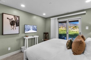 A bedroom with a large bed, a television, a framed picture, and a view of a landscape through a sliding door. - Chatham Crossing 2159 | 2 Living Rooms | Mtn View | Private Patio | Private Garage (Park City)