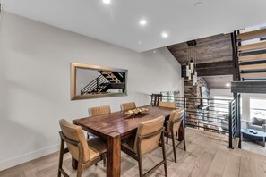 Ein Essbereich mit Holztisch und Stühlen, ein Spiegel mit Spiegelbild der Treppe und eine Treppe mit Metallgeländer.