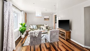 A modern living room with a sofa, two patterned armchairs, a coffee table, a TV on a wooden stand, a large window with curtains, and a potted plant. - Buffalo Bliss - near Universities and natural areas-Large deck and backyard (Duluth)