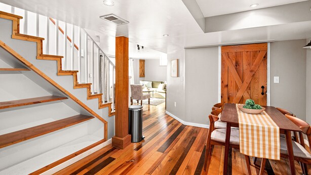 A staircase with wooden steps and white railings, a dining area with a table and chairs, and a wooden door. - Buffalo Bliss - near Universities and natural areas-Large deck and backyard (Duluth)
