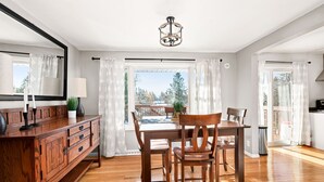 A dining area with a wooden table, chairs, and a cabinet. There is a window with curtains, a chandelier, and a view of trees outside. - Buffalo Bliss - near Universities and natural areas-Large deck and backyard (Duluth)