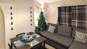 Uma sala de estar acolhedora com uma mesa de jantar posta para dois, um sofá e um pequeno pinheiro de Natal.
