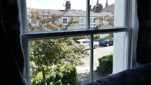 Janela com vista para uma rua residencial, com casas e carros estacionados.