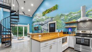 A modern kitchen with a spiral staircase, a large island, and a mural of a forest scene.