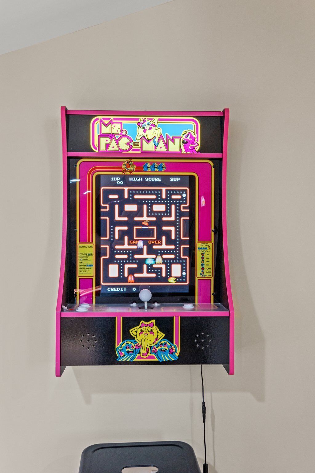 Une borne d’arcade Pac-Man avec un écran affichant le jeu de labyrinthe, un compteur de points et une fente pour les pièces en bas.