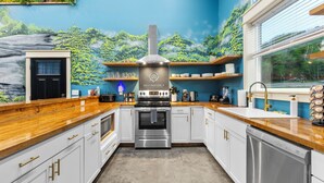 A modern kitchen with white cabinets, stainless steel appliances, and a mural of a forest on the wall.