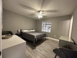 Un dormitorio con cama, escritorio, silla, ventilador de techo y ventana.