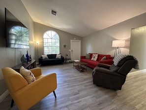Amplia sala de estar con un ventanal grande, un sofá rojo, un sillón amarillo y un sillón oscuro.