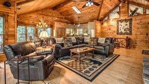 A cozy log cabin interior with a leather sofa set, a chandelier, and a large window.