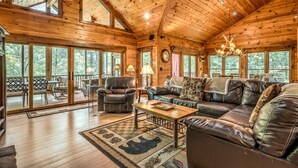 A spacious wooden cabin with a large living area, leather furniture, and large windows offering views of the surrounding forest.