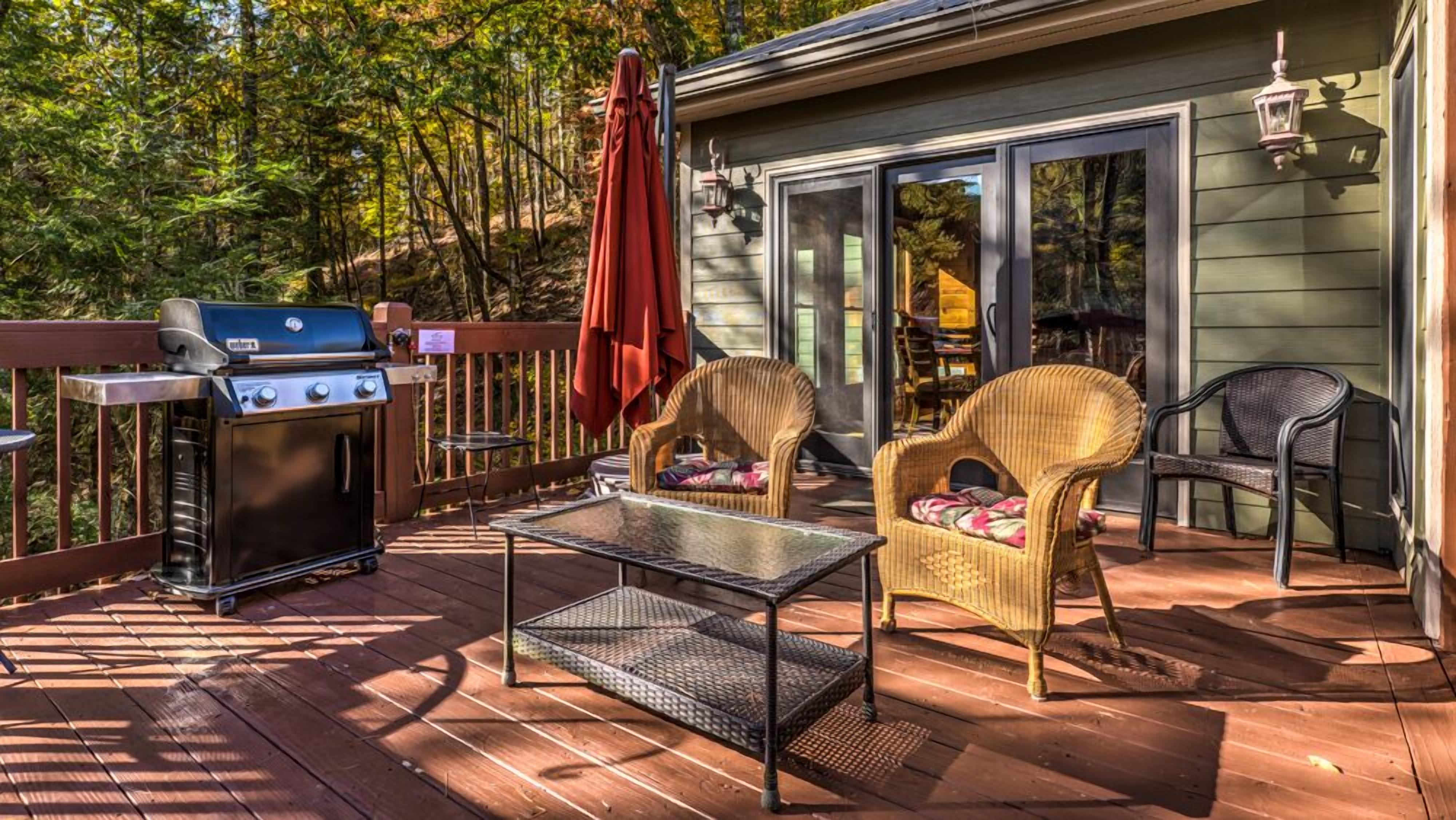 A deck with a grill, wicker chairs, a glass table, and a sliding glass door.