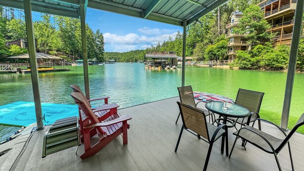A covered outdoor seating area with a table and chairs, overlooking a lake with boats and docked at a pier.
