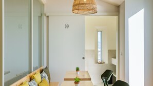 Een modern interieur met een houten eettafel, twee stoelen, een geweven hanglamp en een klein raam.