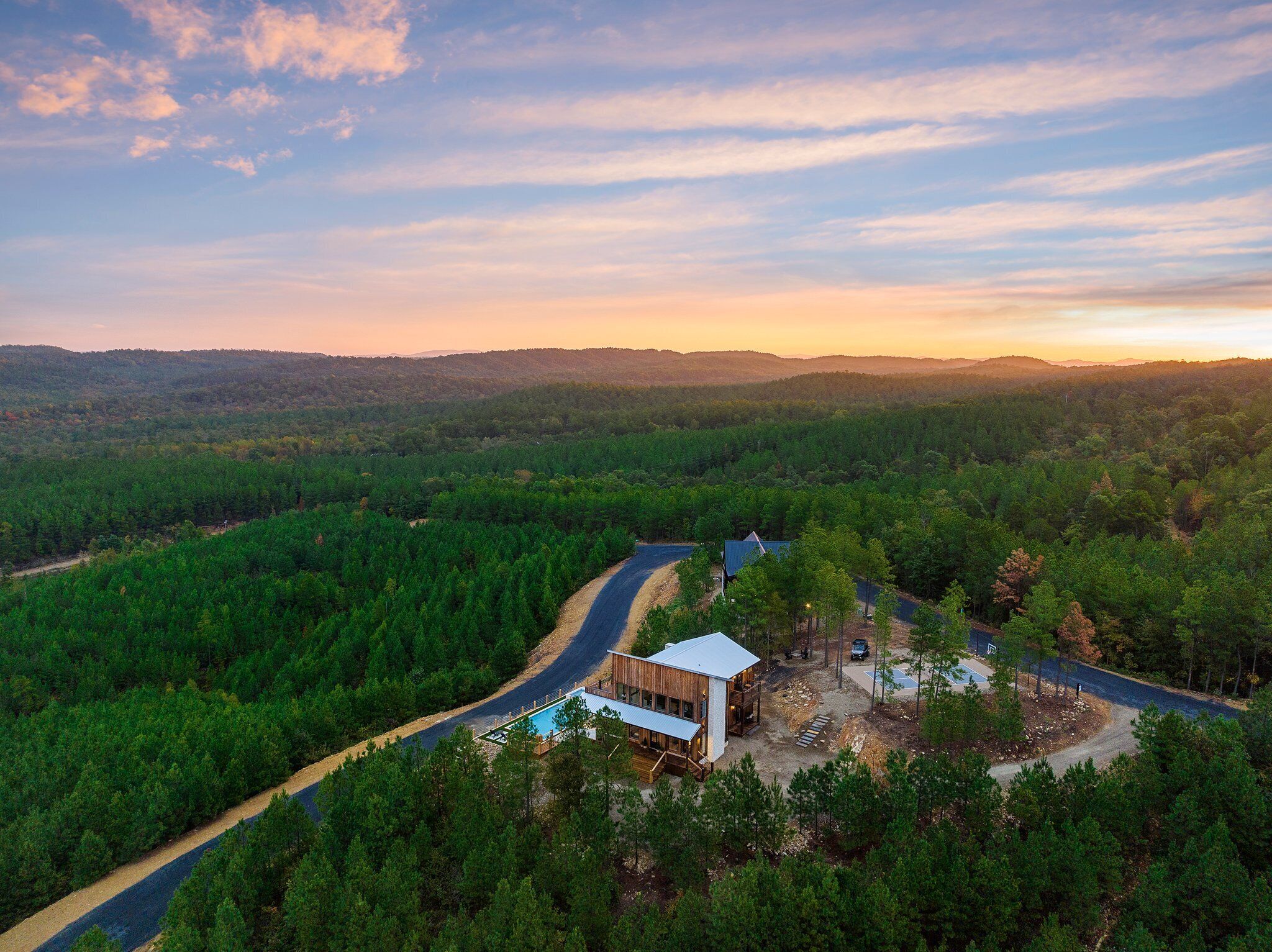 Eine abgelegene Holzhütte mit Pool, umgeben von dichtem Wald und einer kurvigen Straße.