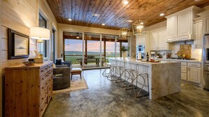 A modern kitchen with a large island, wooden ceiling, and large windows offering a view of the outdoors. - The Overlook w/ Outdoor Pool, EV Outlet, Pickleball, Unbelievable Views (Broken Bow)