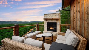 An outdoor deck with a stone fireplace, wicker furniture, and a view of the landscape. - The Overlook w/ Outdoor Pool, EV Outlet, Pickleball, Unbelievable Views (Broken Bow)