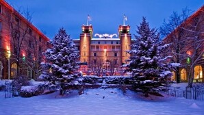 A historic building with two towers, snow-covered trees, and a snow-covered courtyard.