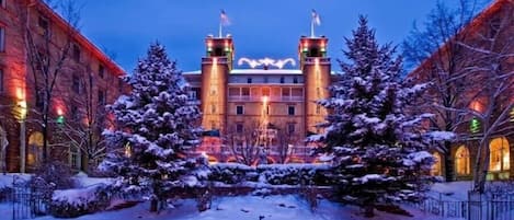 Um edifício histórico com duas torres, árvores cobertas de neve e um pátio coberto de neve.