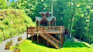 Een houten prieel met een trap, omringd door weelderige begroeiing en bomen.