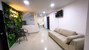 A modern hotel lobby with a reception desk, a beige sofa, a TV mounted on the wall, and a green wall with plants. - Hotel Boutique Veracruz (Santa Rosa de Cabal)