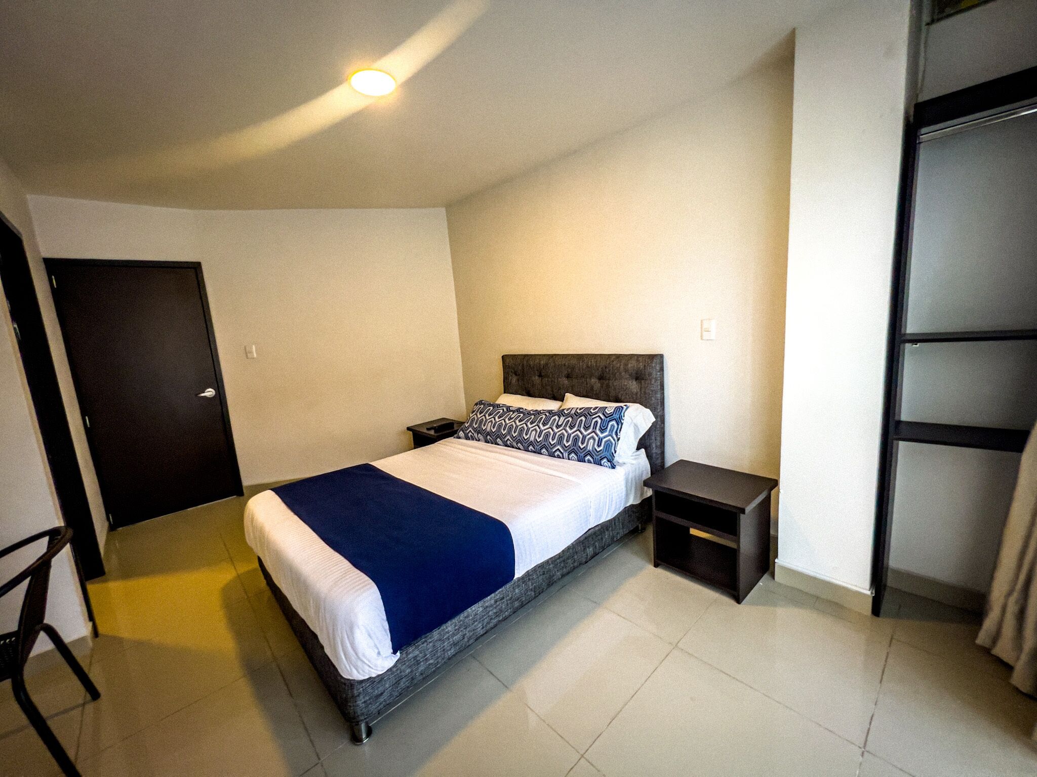 Hotellihuone, jossa on suuri sänky, yöpöytä, tuoli ja vaatekaappi.