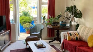 Ein Wohnzimmer mit einer Couch, einem Couchtisch, einem Fernseher und Blick auf einen Garten durch eine Glastür.