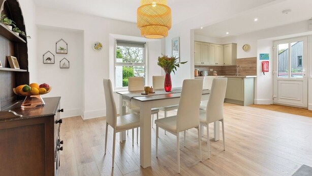 A modern kitchen with white cabinets, a dining area with a white table and chairs, and a hanging light fixture. - Delightful Family Getaway Cornwall (Mawnan Smith)