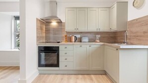 A modern kitchen with light-colored cabinets, a built-in oven, and a coffee maker. - Delightful Family Getaway Cornwall (Mawnan Smith)
