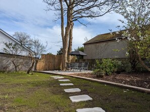 Een achtertuin met een pad van stenen dat leidt naar een terras met tuinmeubels.