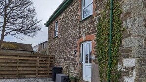A stone building with a white door and a small porch. There is a wooden fence in the background and a tree without leaves. - Delightful Family Getaway Cornwall (Mawnan Smith)
