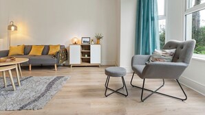 A modern living room with a grey sofa, a grey armchair, a white cabinet, and a small table with a lamp. - Delightful Family Getaway Cornwall (Mawnan Smith)