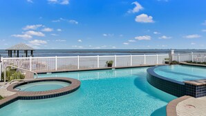 A pool area with a view of the ocean, a gazebo, and a white fence. - Bayfront Home, Shared Pool/Spa, Gazebo, Playground (Port Isabel)