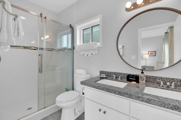 A modern bathroom with a glass-enclosed shower, a white toilet, a double sink vanity, and a large mirror. - Bayfront Home, Shared Pool/Spa, Gazebo, Playground (Port Isabel)