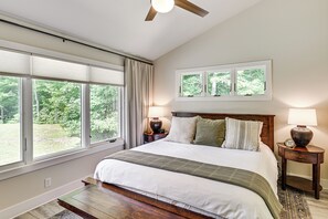 Une chambre avec un grand lit, deux tables de chevet avec des lampes, une fenêtre avec des stores et un ventilateur de plafond.