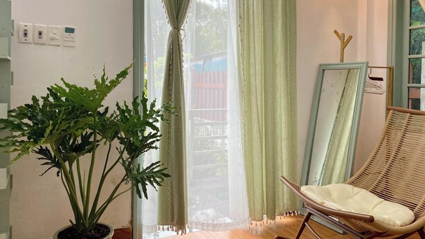 A room with a potted plant, a wicker chair, a mirror, and a window with sheer curtains. - Sunny Balcony, Bathtub, Projector, Chill Chair (Thành phố Huế)