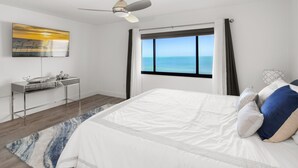 A bedroom with a bed, a desk, a ceiling fan, a window with a view of the ocean, and a painting on the wall. - Get Ready for the Ultimate Beachfront Escape in Naples, Florida! (Naples)