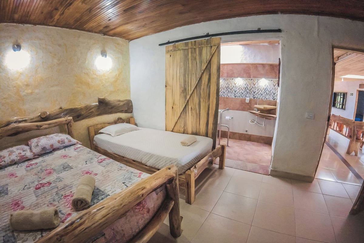 Una habitación rústica de madera con dos camas, un banco de madera, un lavamanos pequeño y vistas a un patio con baldosas.